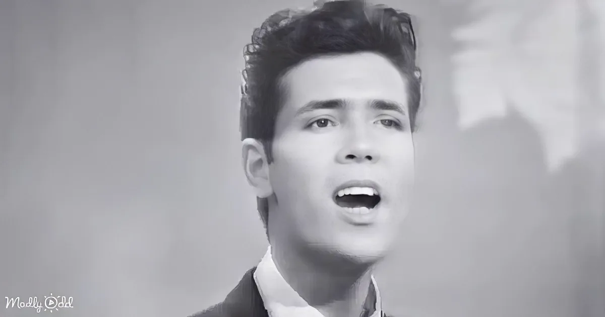 A man in a suit sings passionately, his mouth open, with a blurred background.