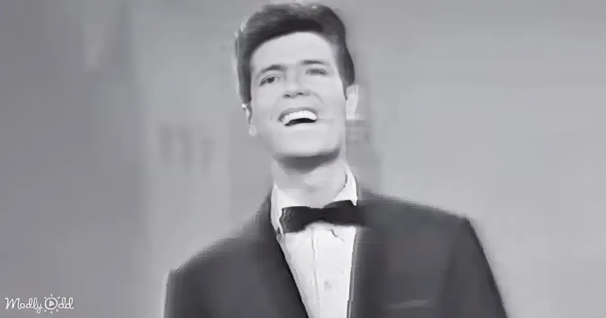 A man in a tuxedo and bow tie smiles, looking upwards, in a black-and-white image.