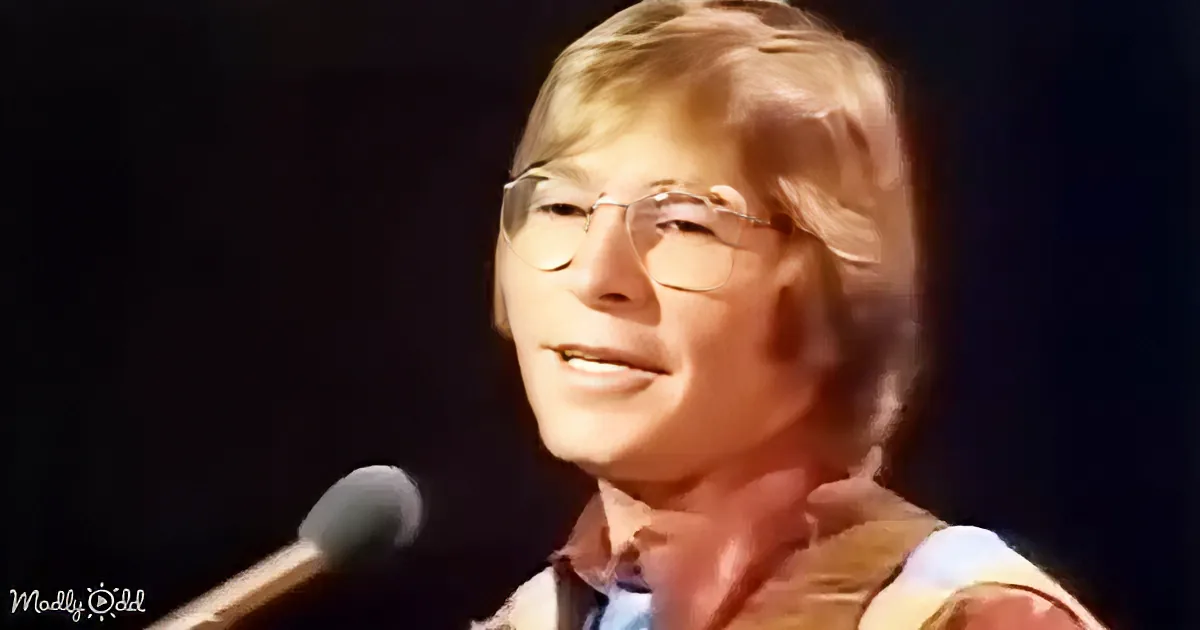 A smiling person with glasses and a striped shirt is speaking into a microphone.