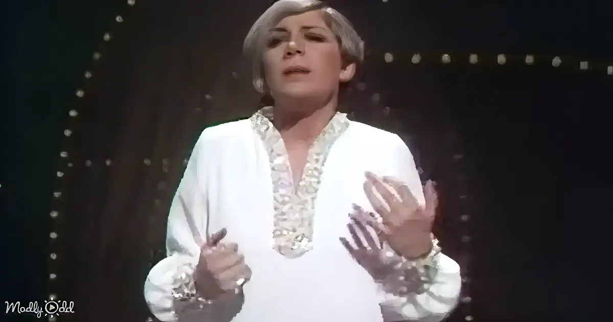 A person in a white outfit with intricate details is holding scissors and gesturing with their hands.