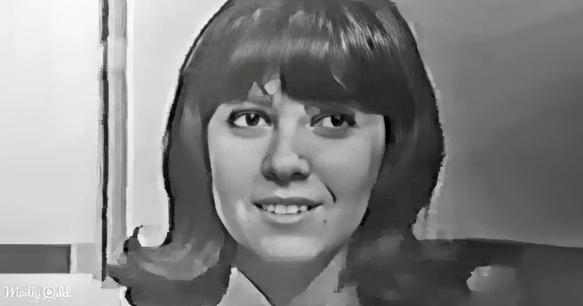 A smiling woman with shoulder-length hair and bangs, wearing a white top, in a black-and-white setting.
