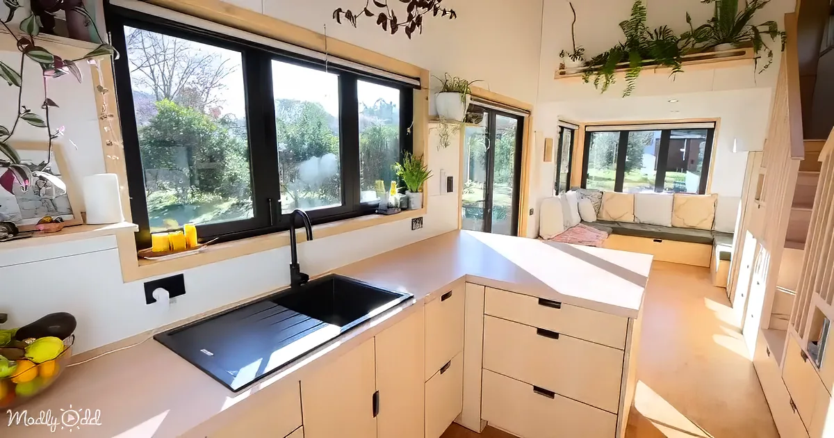A cozy, well-lit kitchen with a large window, white cabinets, a black sink, and a view of greenery outside.