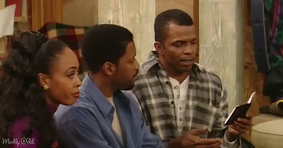 A man in a plaid shirt holds a book, while another man in a blue shirt and a woman with curly hair look on.