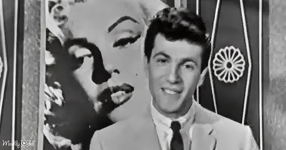 A man in a suit smiles in front of a large, stylized face backdrop.