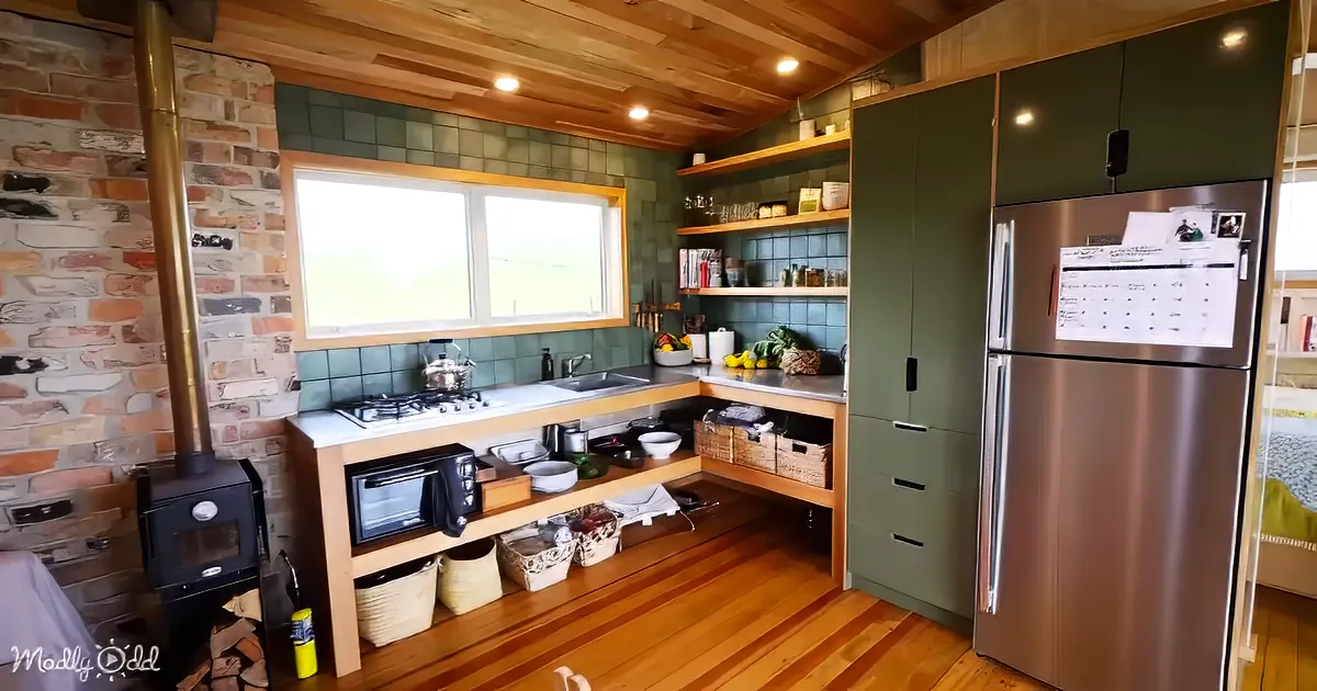 A cozy kitchen with wooden floors, green cabinets, a brick wall, and a small stove.