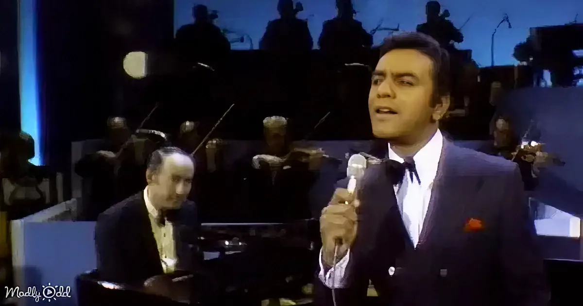 A man in a suit sings into a microphone, accompanied by an orchestra in the background.