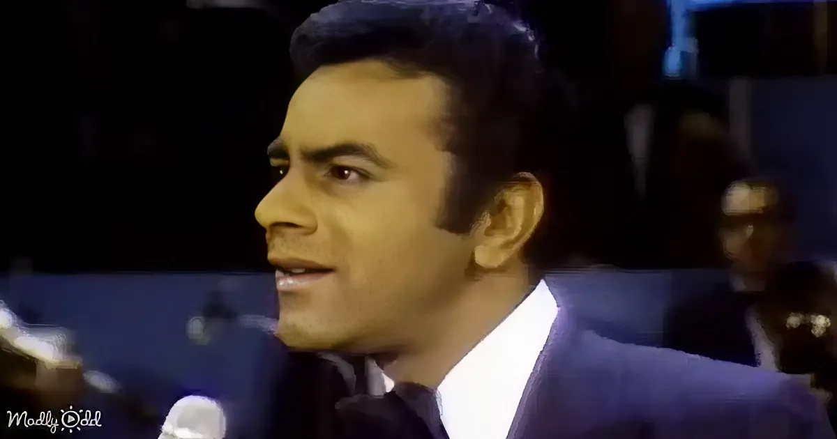 A man in a suit and tie smiles while speaking into a microphone.