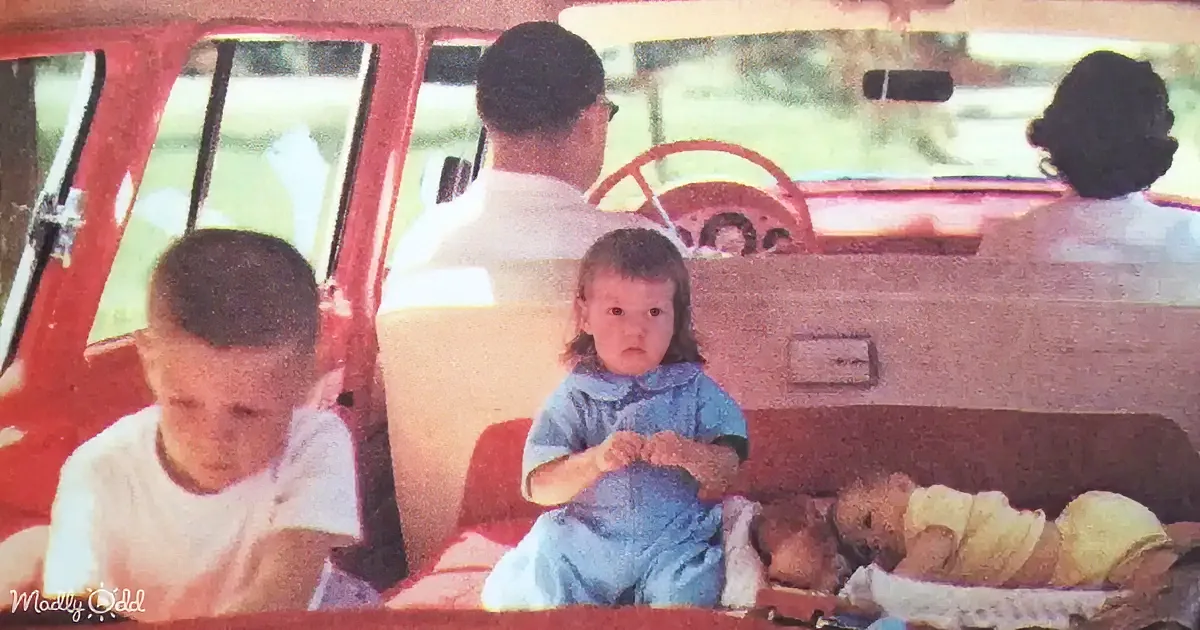 A family is in a vintage car, with a child in the back seat looking forward.