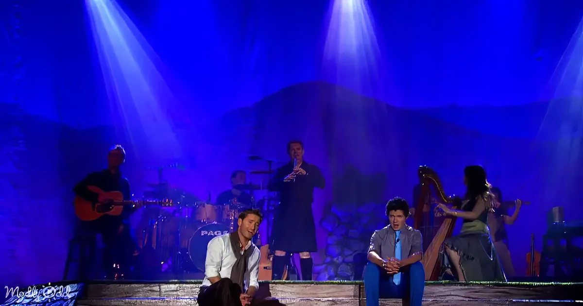 A musician plays a flute on stage with a group of musicians and a harpist, under blue stage lights.