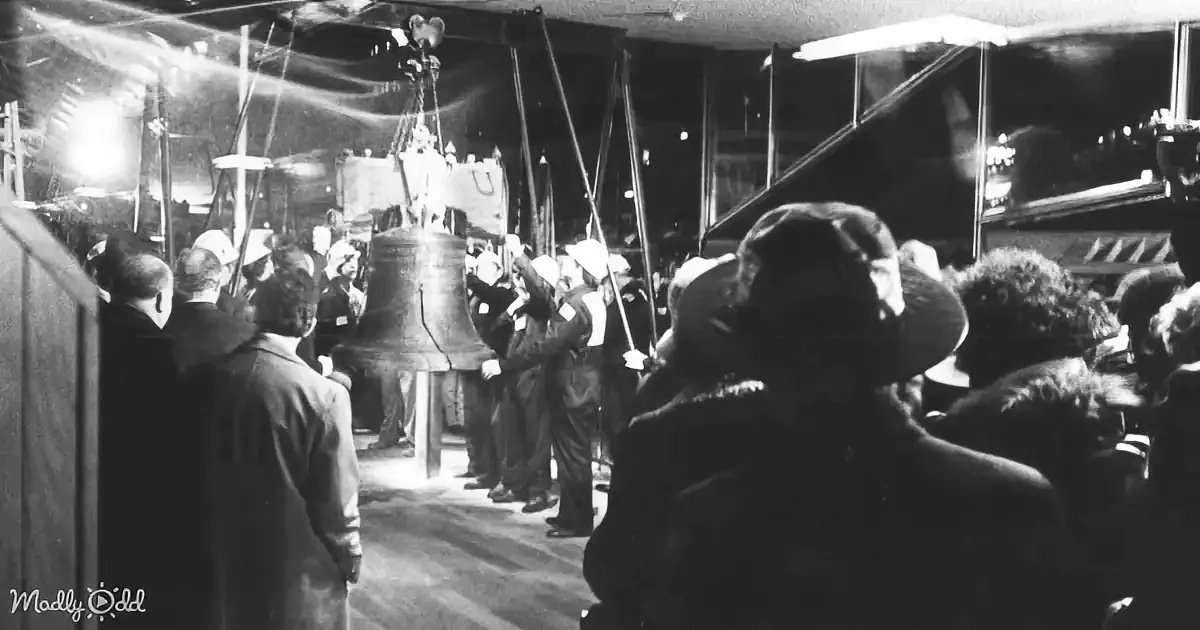 A group of people stands around a large bell, possibly during a ceremony or event.