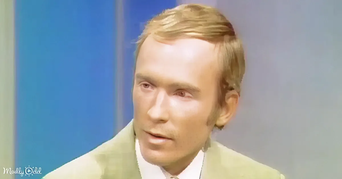 A man with light brown hair, wearing a light-colored suit, is looking to the side.