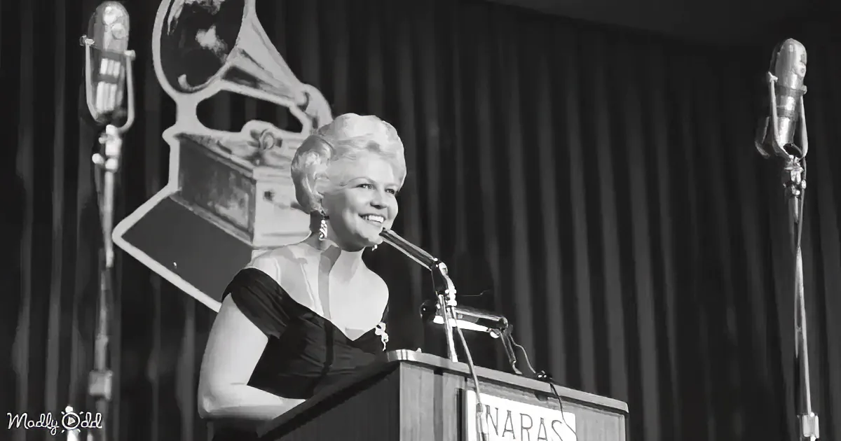A woman in a black dress smiles at a podium with a gramophone in the background.