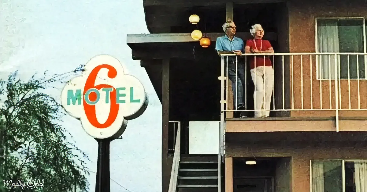 Two people stand on a motel balcony, enjoying the view near a Motel 6 sign.