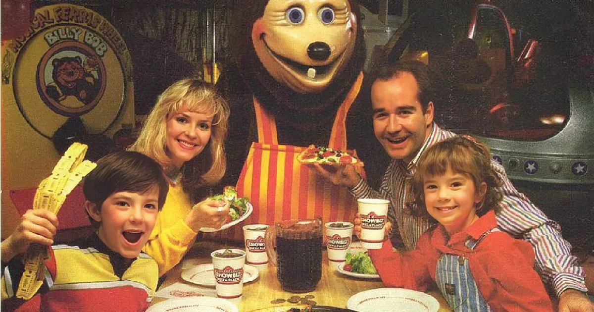 Family dining with mascot, enjoying pizza and drinks at Showbiz Pizza Place.