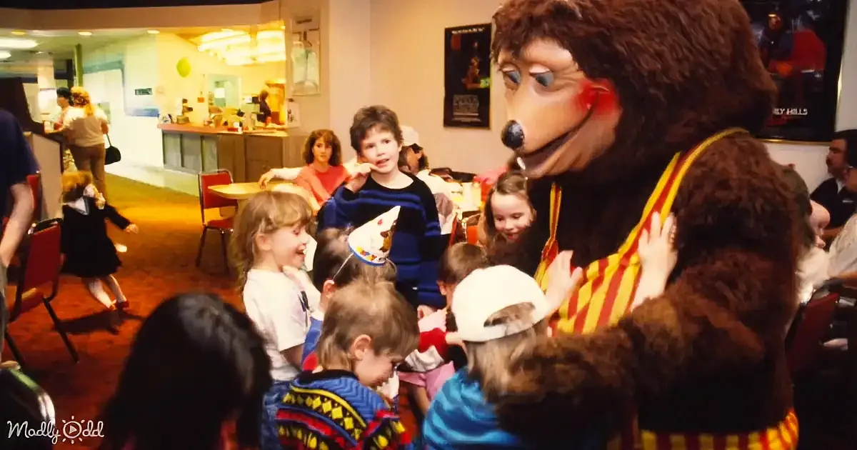 A person in a bear costume interacts with children in a lively indoor setting.