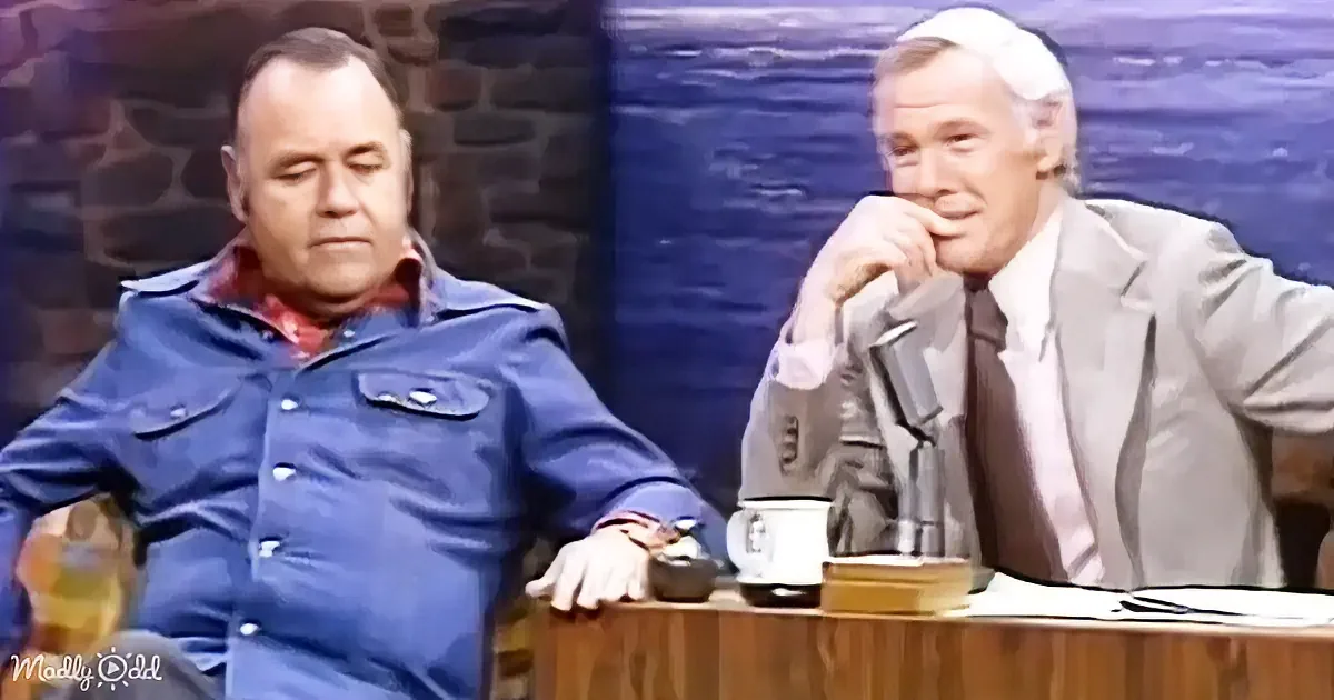 A man in a blue jacket sits at a desk with a coffee mug, while another man in a suit leans back, hand on chin.