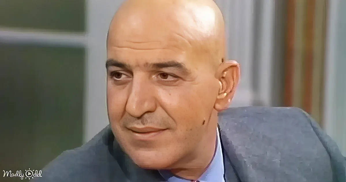 A bald man in a suit and tie, looking to the side with a serious expression.