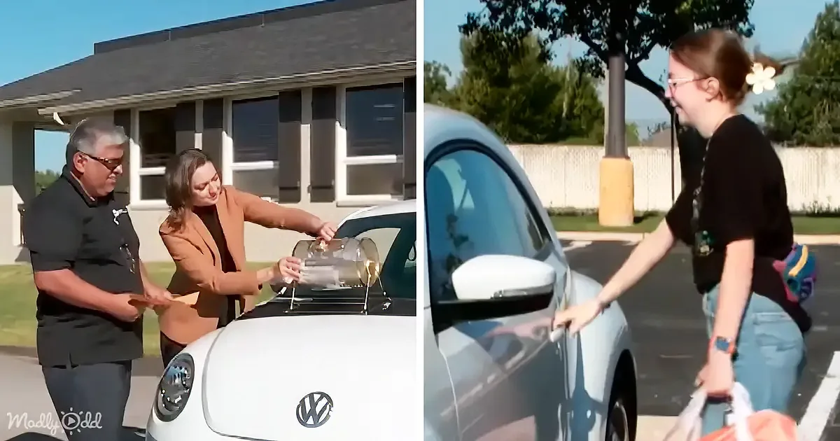 A woman hands a clear object to a man near a white Volkswagen Beetle, while another woman points at the car's door.