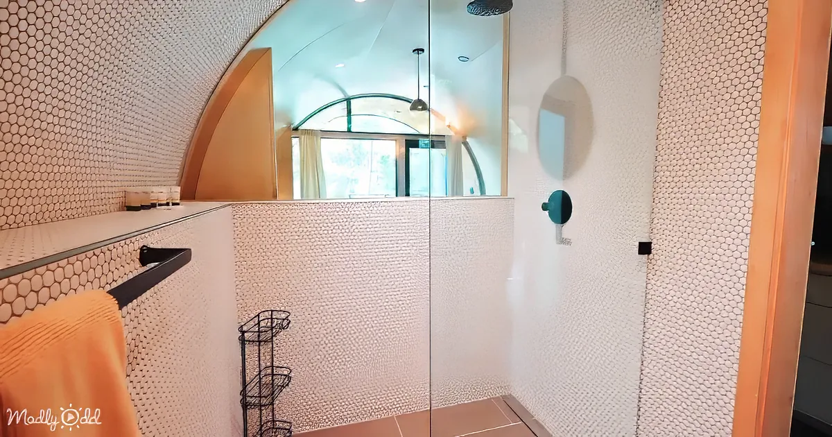 A modern bathroom with hexagonal tiles, a glass shower, and a curved window.