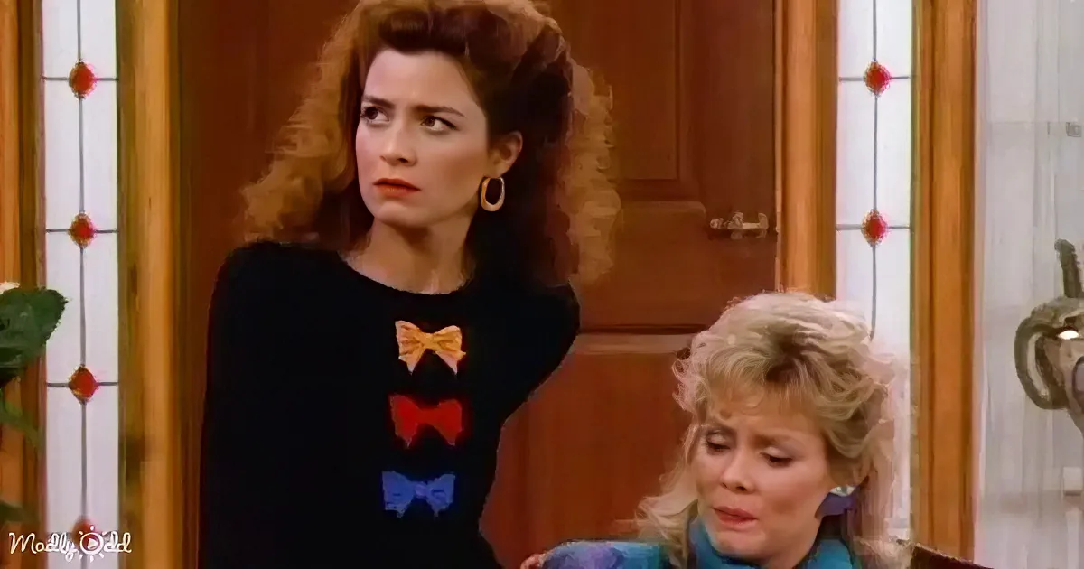 A woman in a black sweater with colorful bow designs stands next to another woman with blonde hair in a room with wooden...