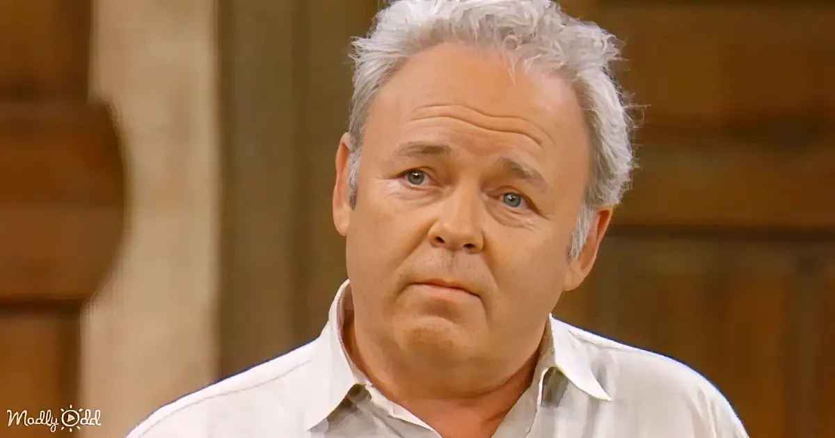 A man with gray hair and a white shirt looks slightly to the side, with a neutral expression.