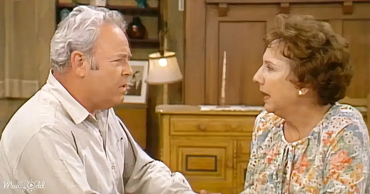 A man and woman are having a conversation in a warmly lit room with wooden furniture.