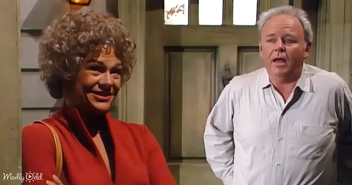 A woman in a red outfit smiles while a man in a white shirt stands beside her, both in a room with a door and window.