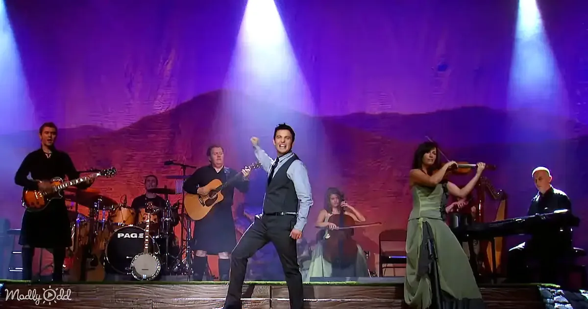 A man in a suit dances energetically on stage with a band and musicians.