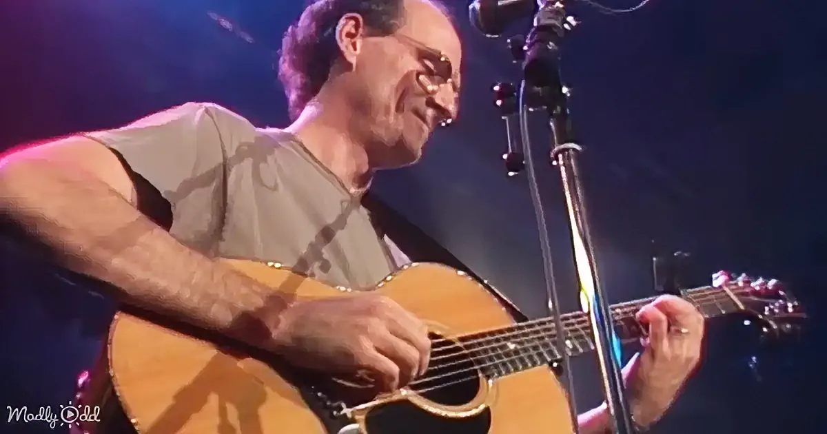 A man with glasses sings into a microphone, illuminated by blue stage lights.