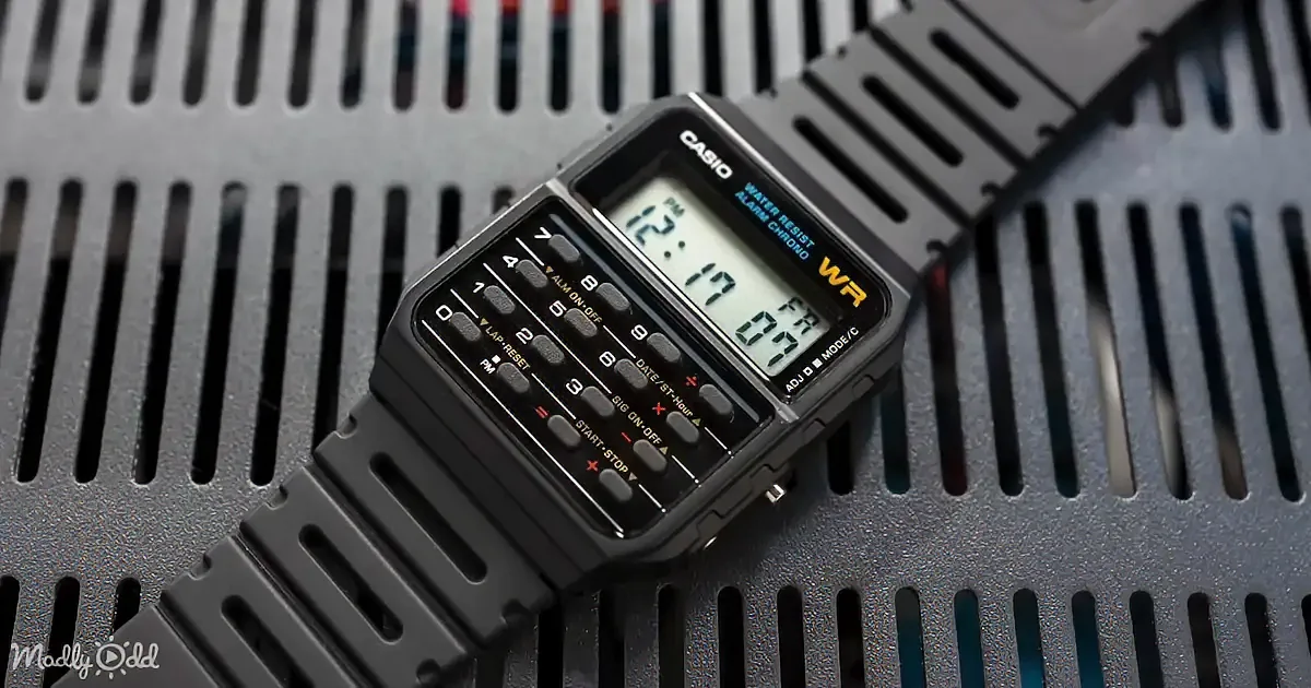 A Casio digital watch with a black face and buttons, displaying time and date, rests on a textured gray surface.