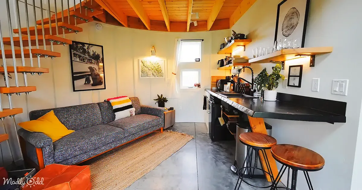 A cozy living space with a grey couch, orange accents, and a modern kitchen with bar stools.