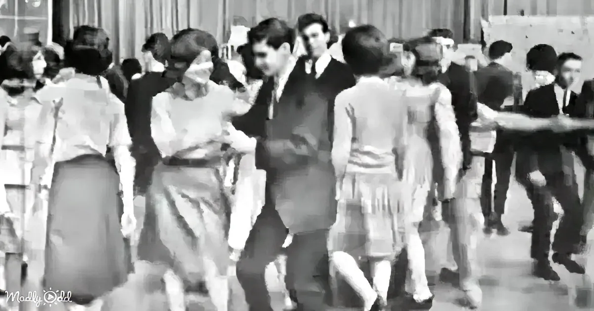 A man in a suit dances with a woman in a dress at a lively social event.