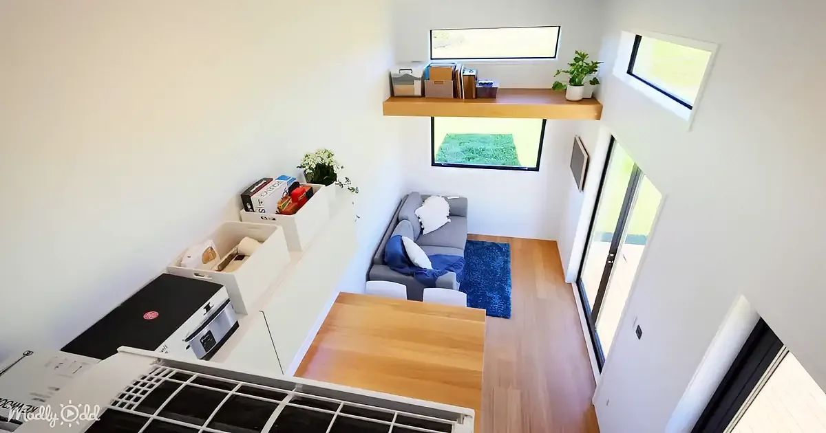 A cozy living space with a small sofa, wooden table, and storage boxes, featuring a skylight and a sliding glass door.