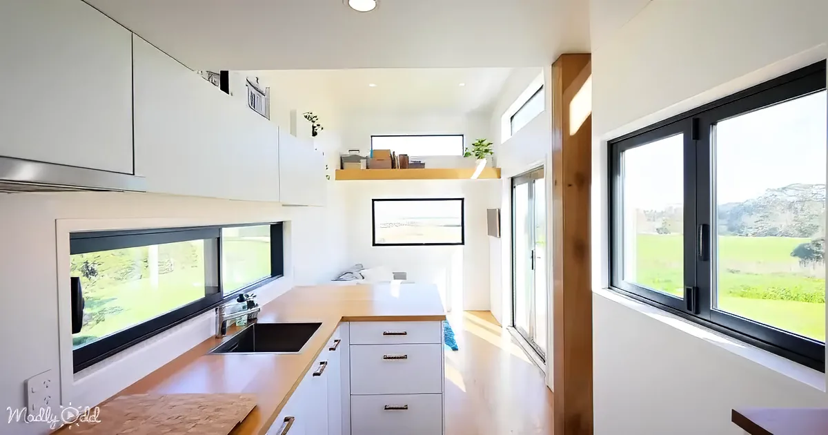 A modern kitchen with white cabinets, wooden countertops, and large windows offering a view of greenery.