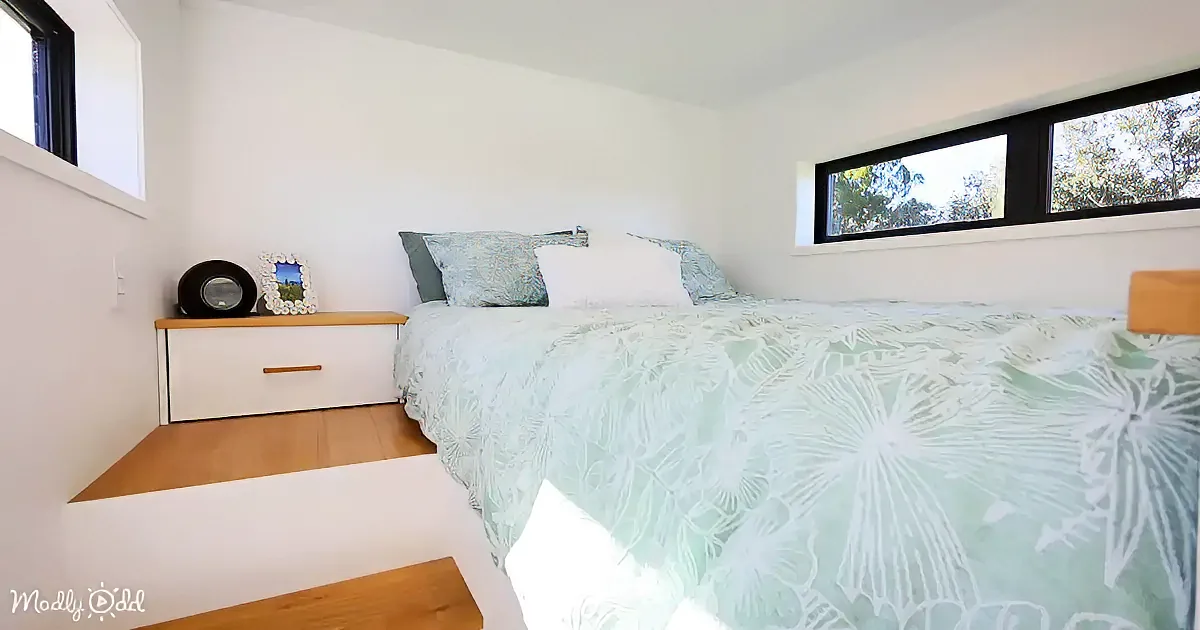 A neatly made bed with a green and white patterned duvet, white pillows, and a wooden nightstand with a framed picture...