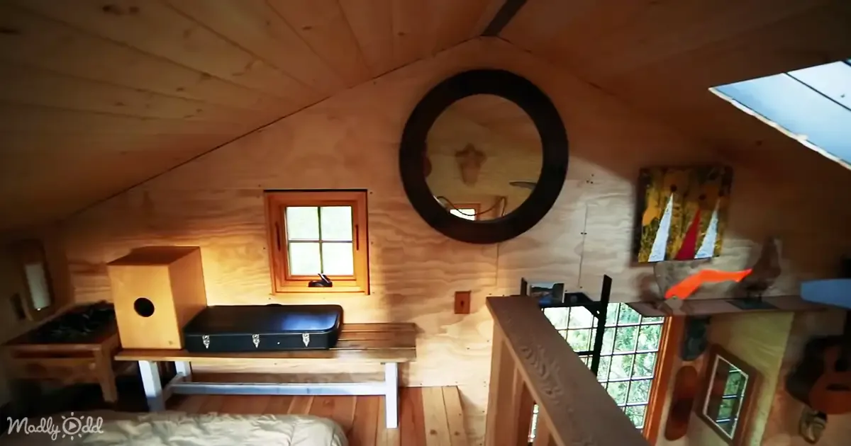 A cozy wooden cabin interior with a round mirror, small window, and wooden furniture.