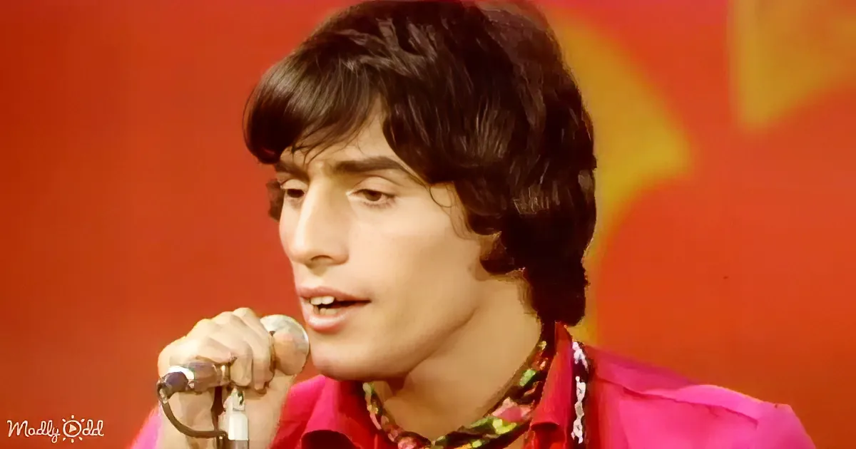 A person in a vibrant red shirt sings into a microphone against a red background.