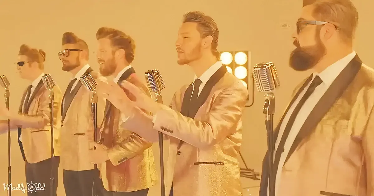 A man in a shiny gold suit sings into a microphone, surrounded by other men in similar attire.