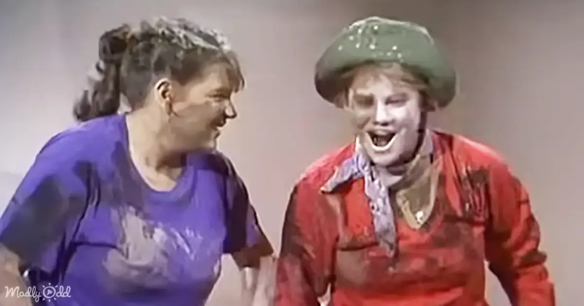 A person in a red outfit with a green hat and another person in a blue shirt with a messy ponytail are interacting.