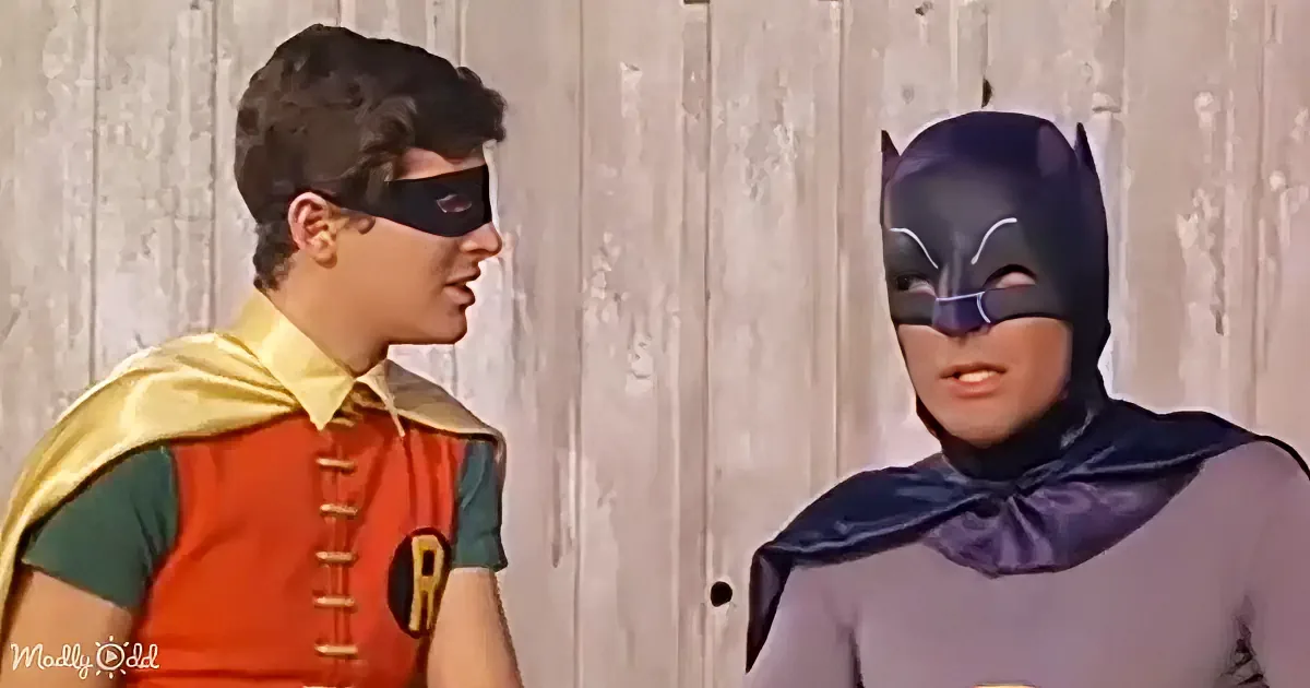 Batman and Robin in their iconic costumes stand facing each other against a wooden backdrop.