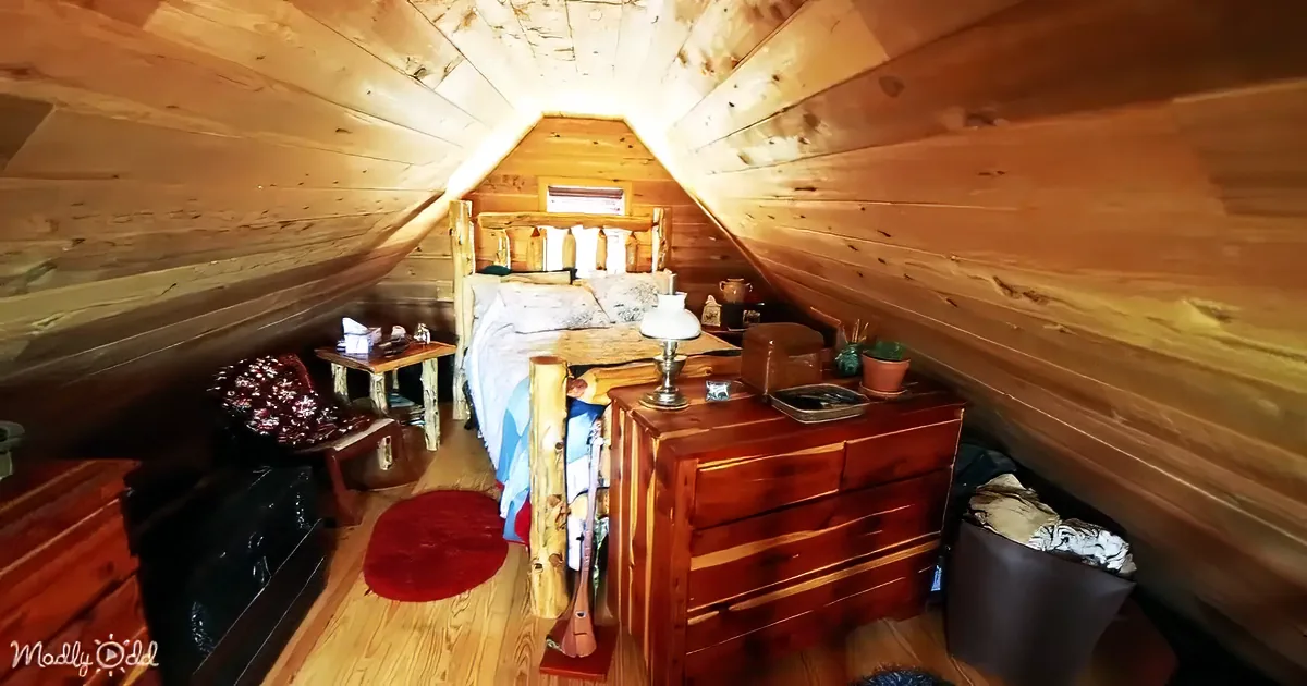 A cozy attic bedroom with wooden walls, a bed, dresser, and a red rug on the floor.