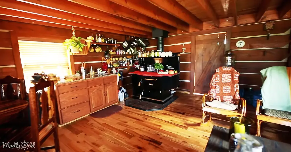 A cozy cabin interior with wooden walls, a kitchen counter, and a chair with a patterned cover.
