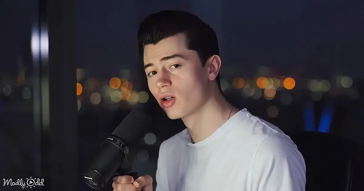 A person in a white shirt sings into a microphone against a cityscape backdrop.