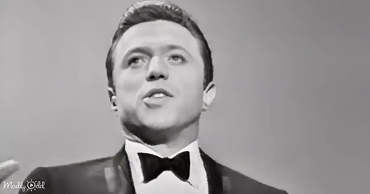 A man in a tuxedo and bow tie is singing, looking upwards, with a microphone visible.