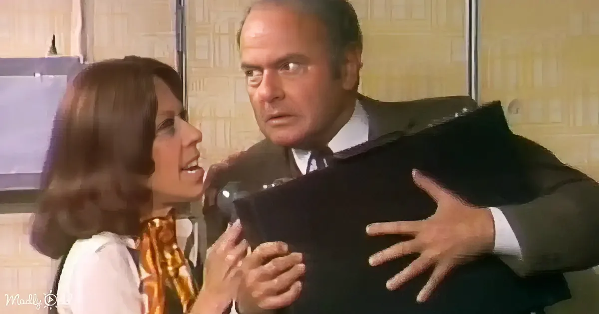 A man in a suit is being held by a woman in a white blouse and gold scarf.