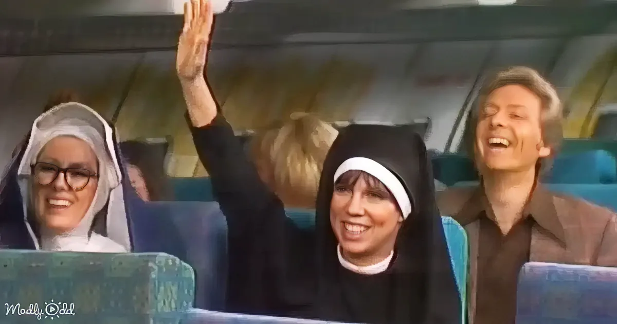A nun in a black habit raises her hand in the air, smiling, with other people in the background.