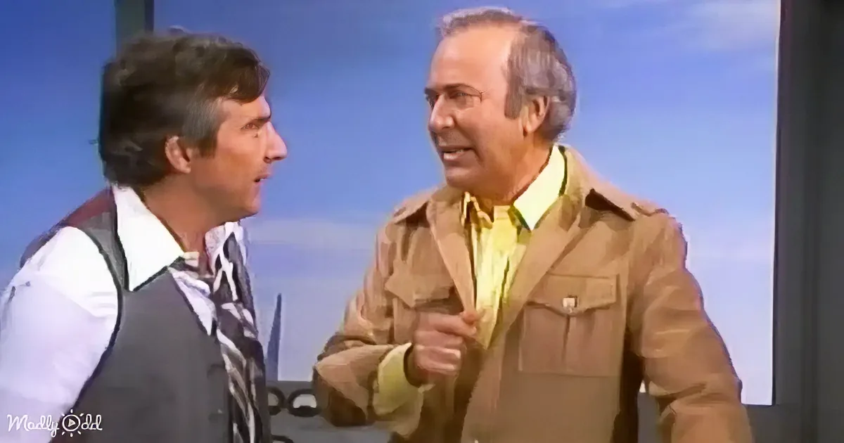 Two men in conversation, one in a tan jacket and yellow shirt, the other in a vest and striped tie.