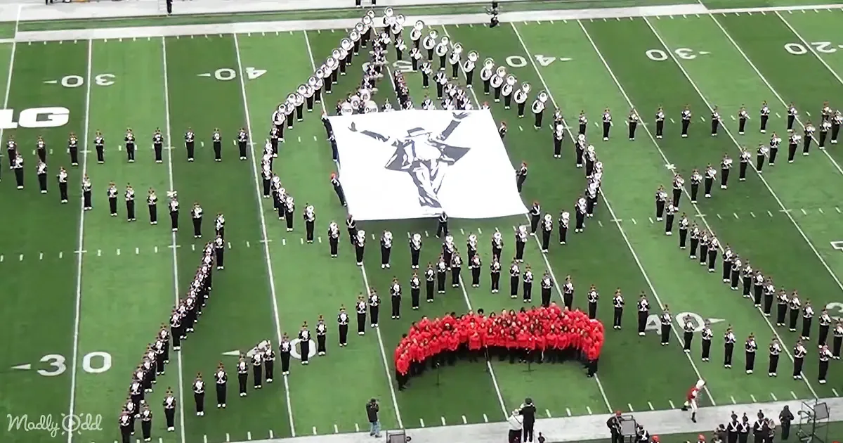 A marching band forms a detailed image on a football field, with a large white figure at the center.