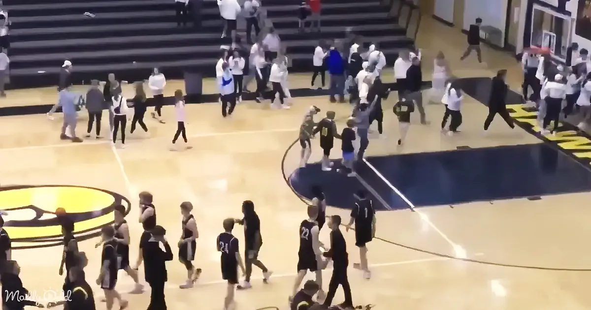Young basketball players in black uniforms walk off court, surrounded by spectators and other players.