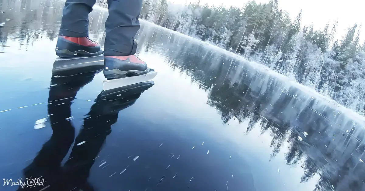 A person ice skating on a frozen lake with a snowy forest reflection.